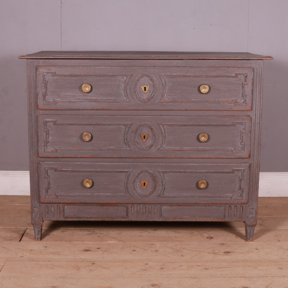 A French Neoclassical grey-painted three-drawer commode featuring geometric drawer moldings, brass hardware, and fluted legs. View IV