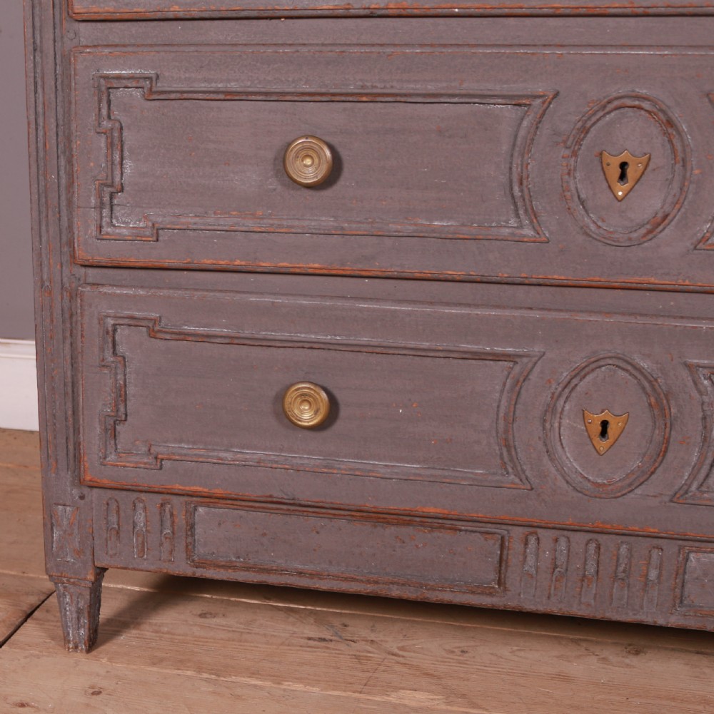 A French Neoclassical grey-painted three-drawer commode featuring geometric drawer moldings, brass hardware, and fluted legs. View V
