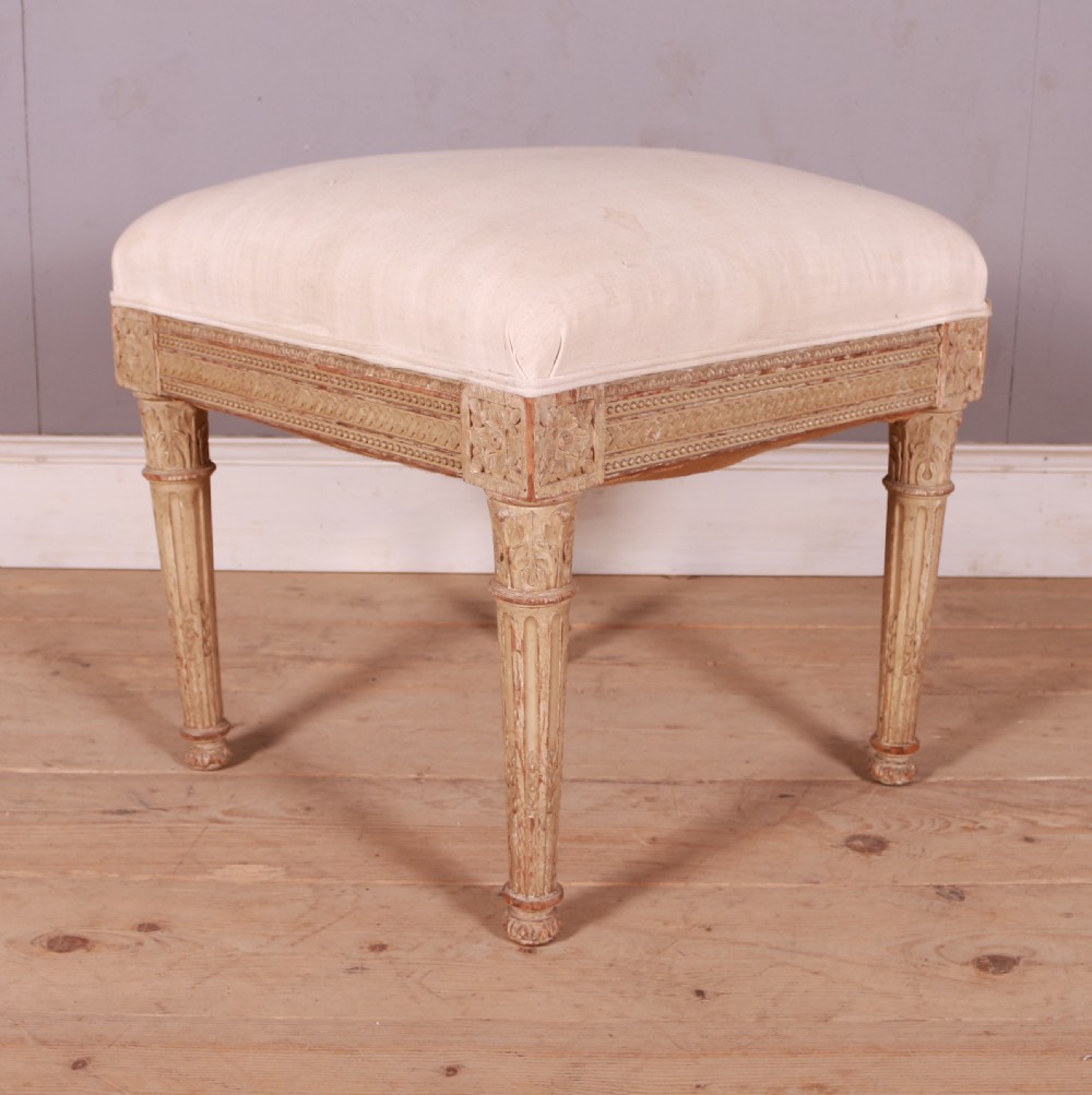 A square Swedish Gustavian upholstered stool featuring distressed cream painted wood legs with fluted carving and a light linen seat. View IV