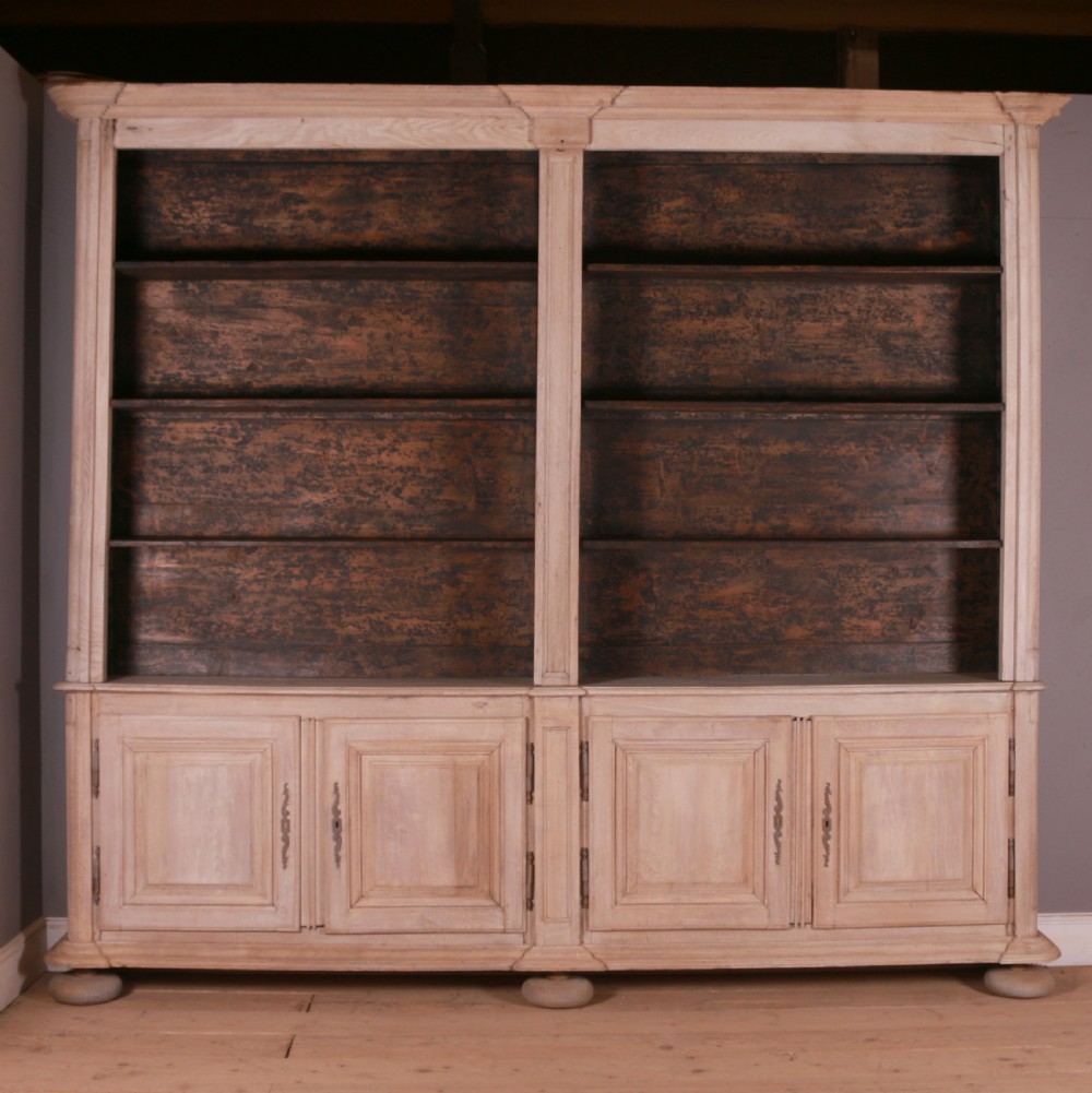 An 18th-century French bleached oak bookcase featuring upper open shelving against dark backboards and a lower section with four fielded panel doors.