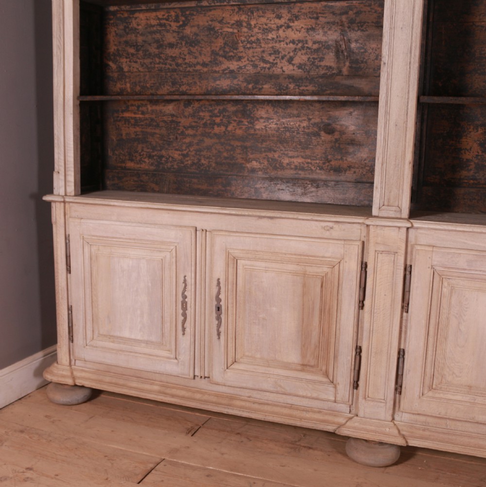 An 18th-century French bleached oak bookcase featuring upper open shelving against dark backboards and a lower section with four fielded panel doors. View V