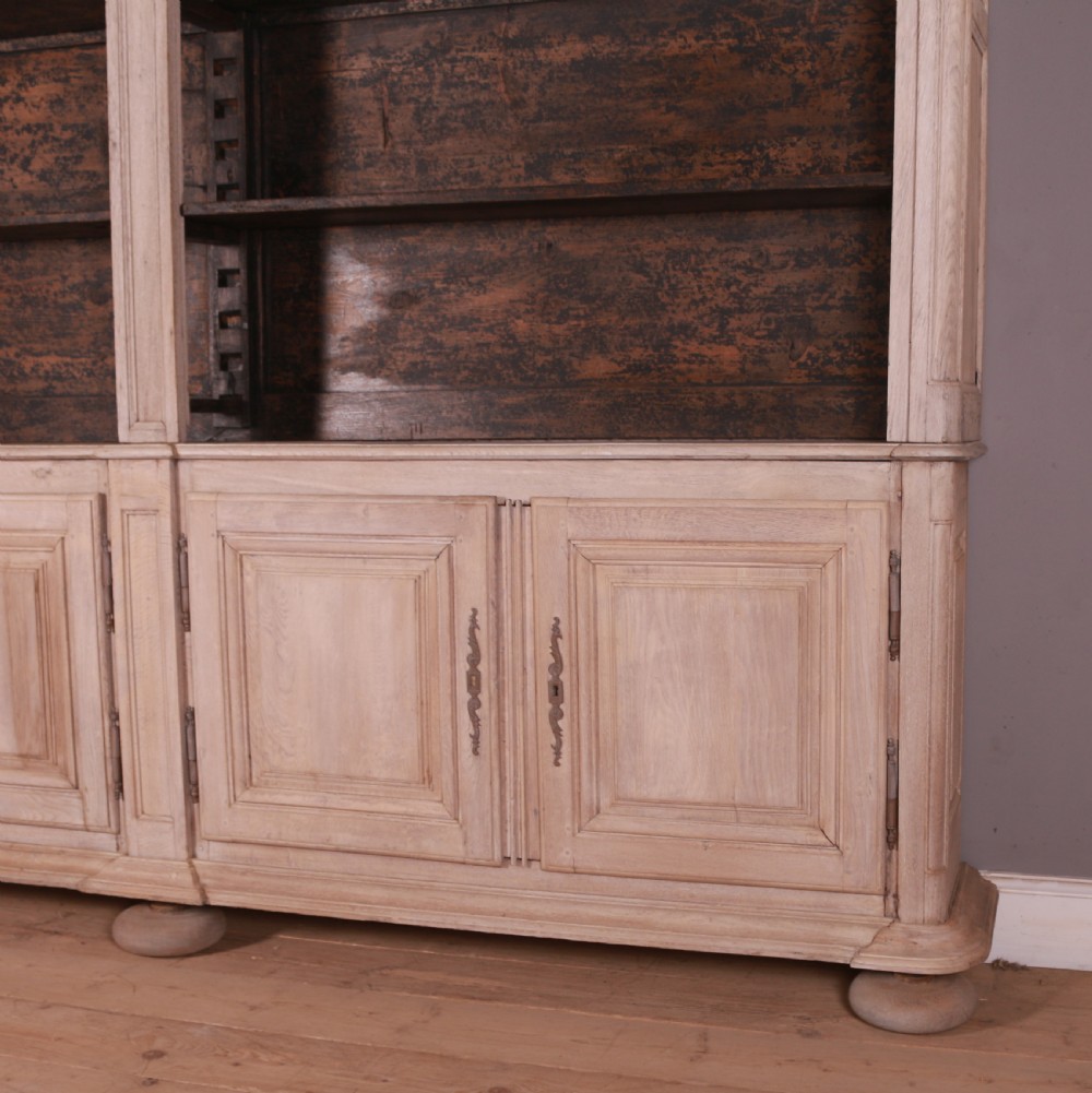 An 18th-century French bleached oak bookcase featuring upper open shelving against dark backboards and a lower section with four fielded panel doors. View VI