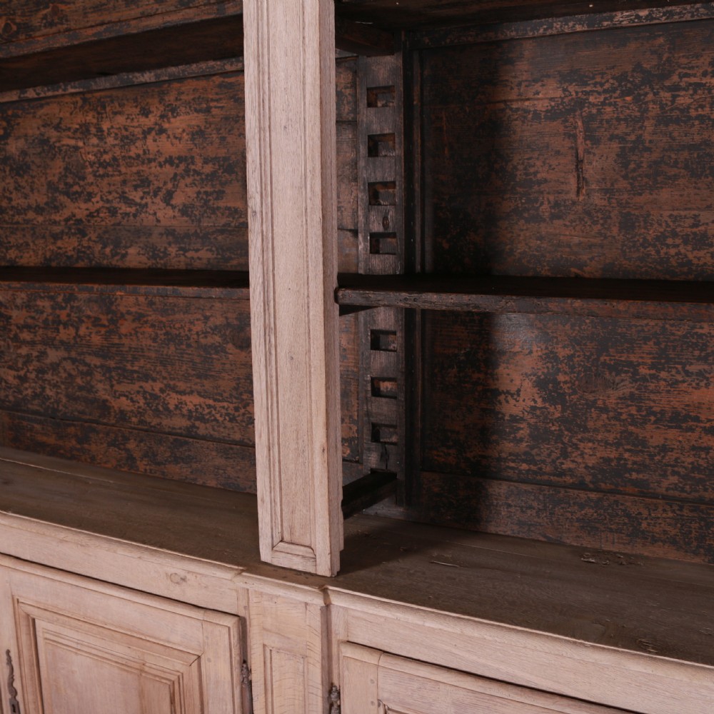 An 18th-century French bleached oak bookcase featuring upper open shelving against dark backboards and a lower section with four fielded panel doors. View IX