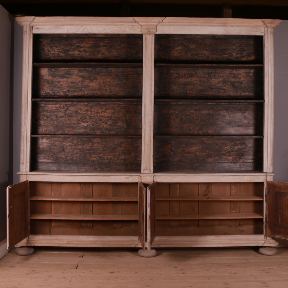 An 18th-century French bleached oak bookcase featuring upper open shelving against dark backboards and a lower section with four fielded panel doors. View X