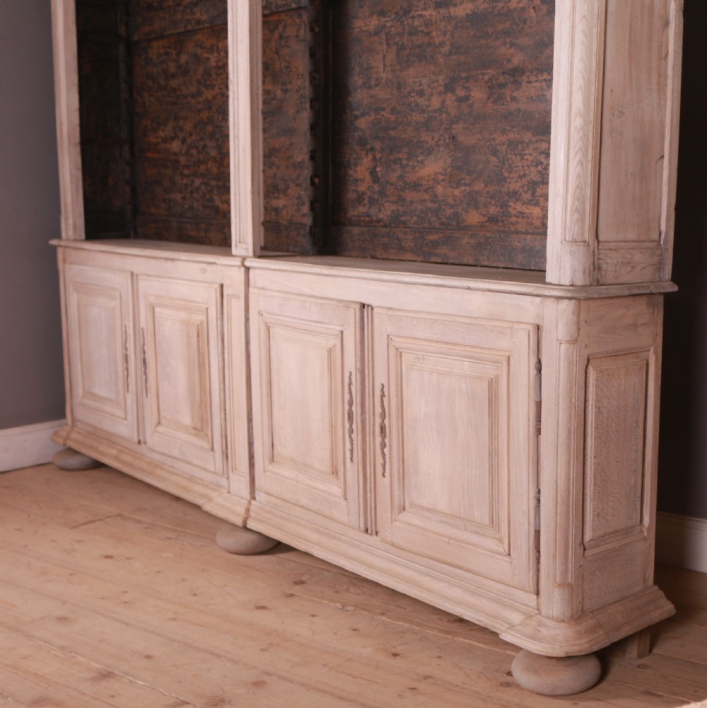 An 18th-century French bleached oak bookcase featuring upper open shelving against dark backboards and a lower section with four fielded panel doors. View XI