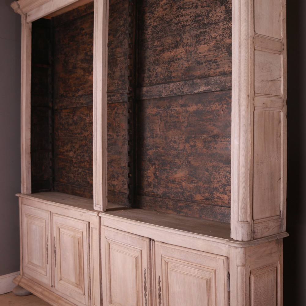 An 18th-century French bleached oak bookcase featuring upper open shelving against dark backboards and a lower section with four fielded panel doors. View XII