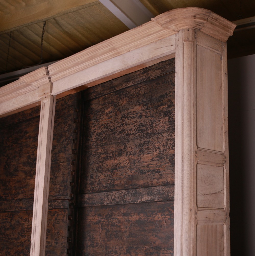 An 18th-century French bleached oak bookcase featuring upper open shelving against dark backboards and a lower section with four fielded panel doors. View XIII