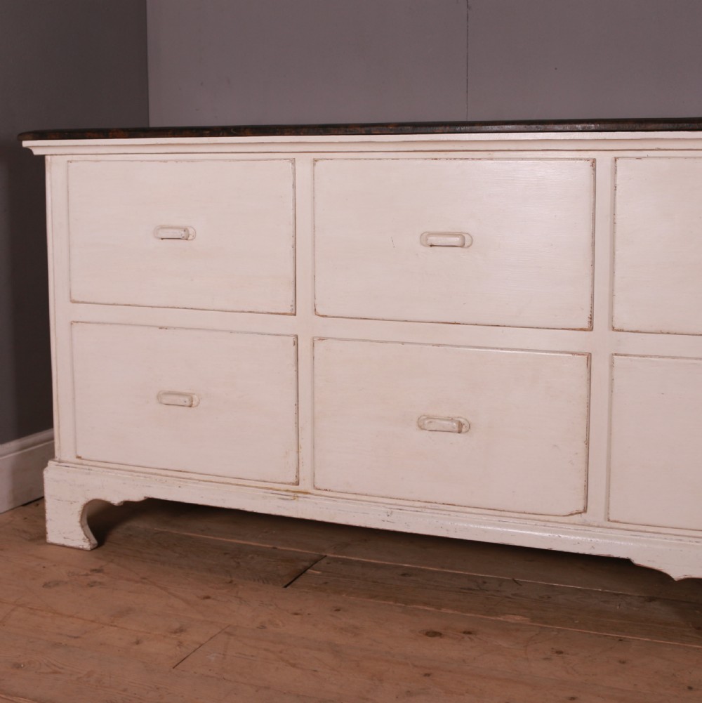 A long off-white painted French bank of drapers drawers featuring ten large drawers with wooden handles and a dark stained top surface. View II