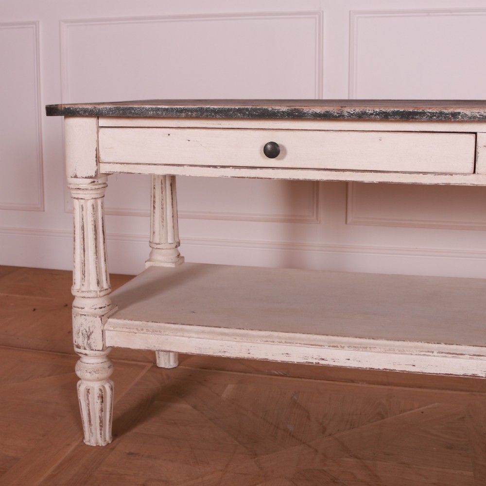 A cream painted pine side table featuring two drawers, turned fluted legs, a lower open shelf, and a dark contrasting top. View III