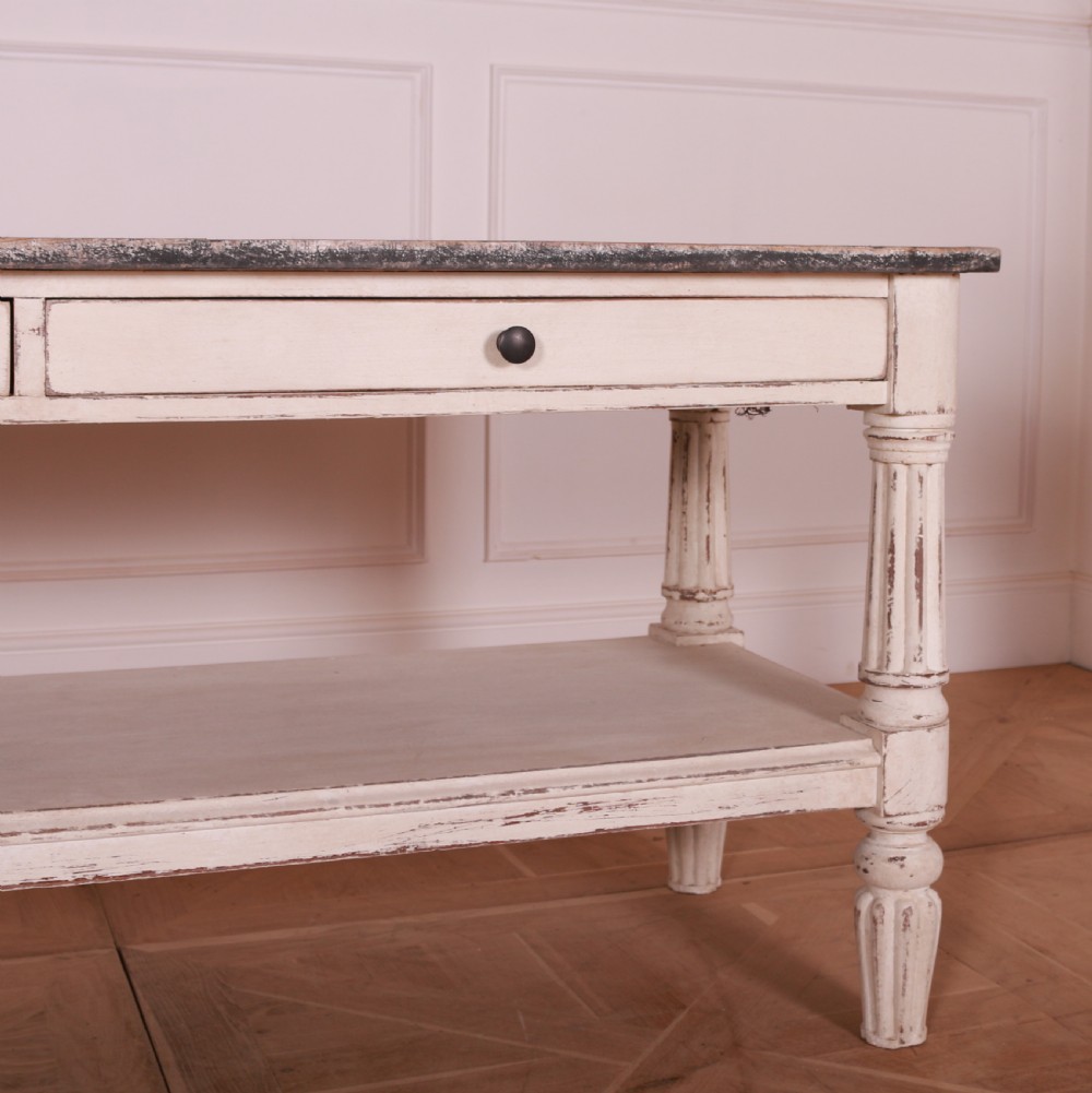 A cream painted pine side table featuring two drawers, turned fluted legs, a lower open shelf, and a dark contrasting top. View V
