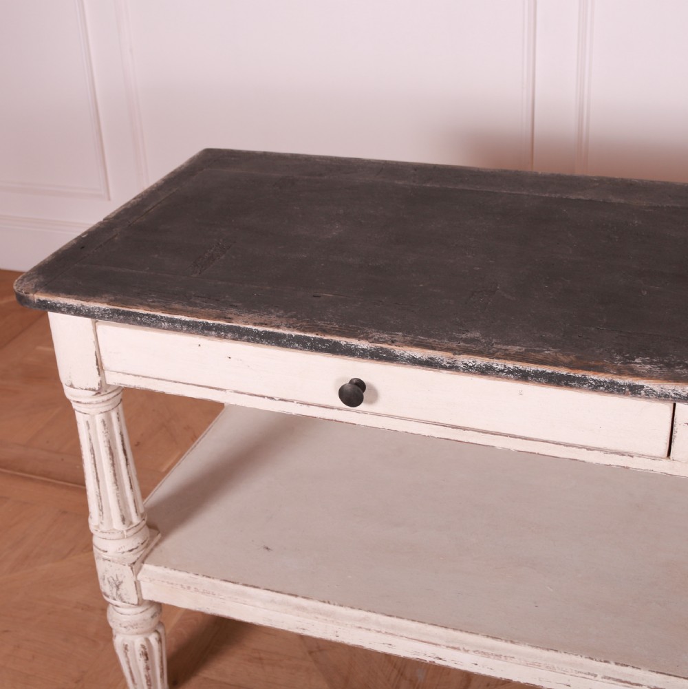A cream painted pine side table featuring two drawers, turned fluted legs, a lower open shelf, and a dark contrasting top. View VII