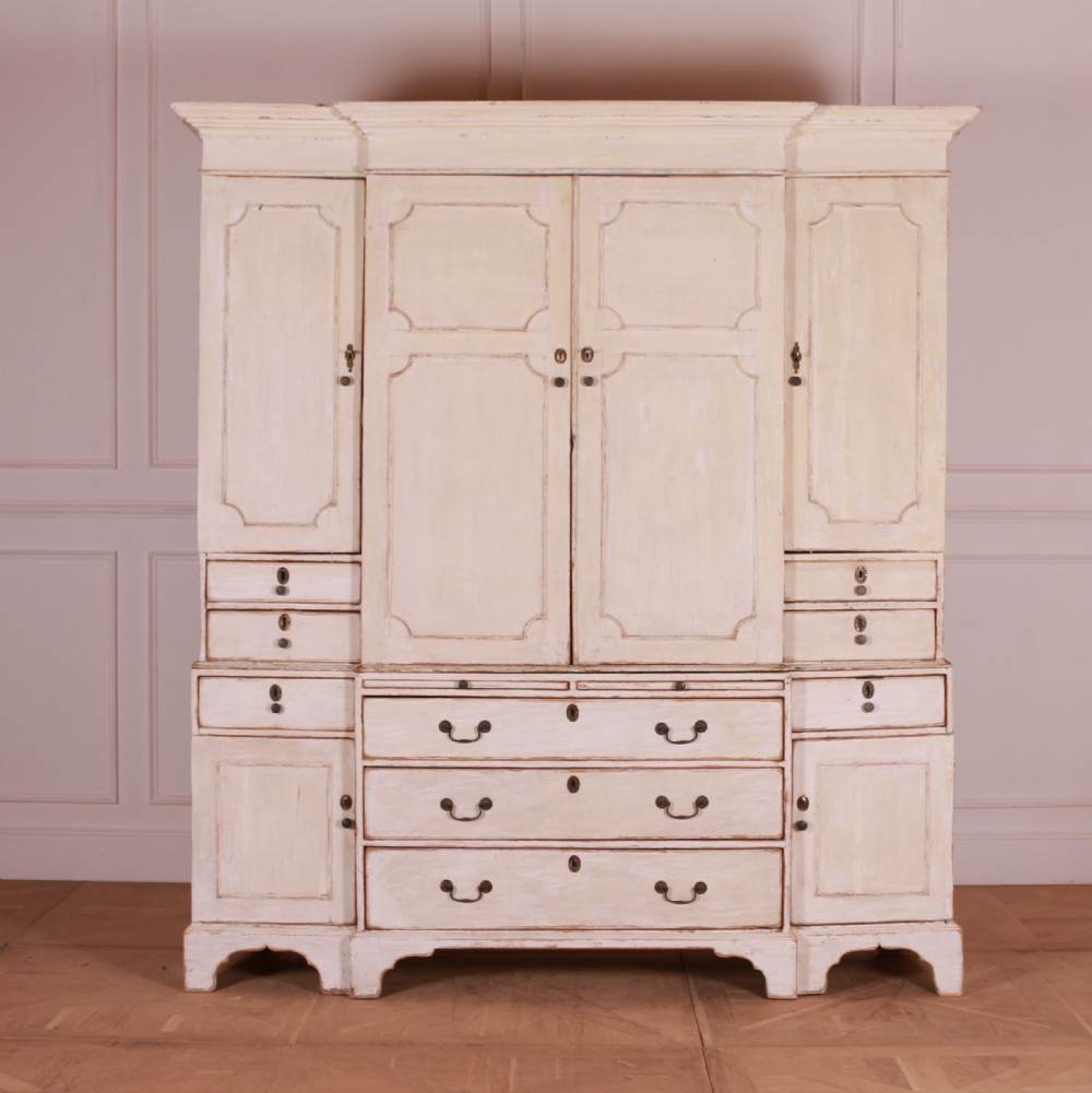 An eighteenth-century off-white painted housekeepers cupboard featuring fielded panel cupboard doors above multiple drawers with brass handles, supported by bracket feet.