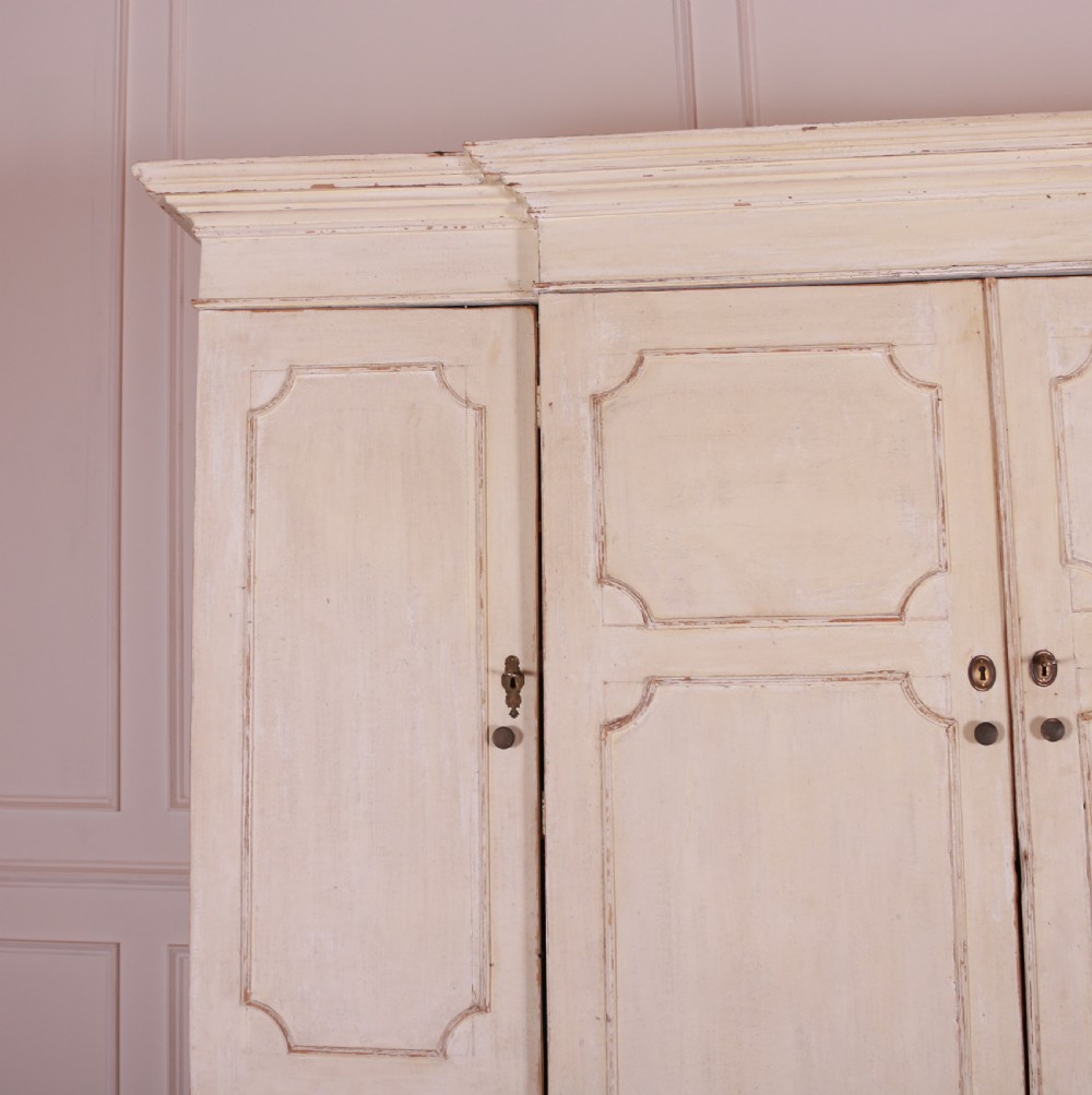 An eighteenth-century off-white painted housekeepers cupboard featuring fielded panel cupboard doors above multiple drawers with brass handles, supported by bracket feet. View II