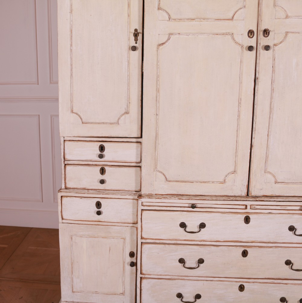 An eighteenth-century off-white painted housekeepers cupboard featuring fielded panel cupboard doors above multiple drawers with brass handles, supported by bracket feet. View III
