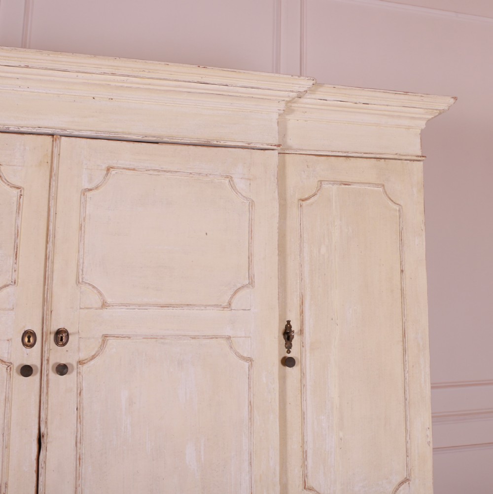 An eighteenth-century off-white painted housekeepers cupboard featuring fielded panel cupboard doors above multiple drawers with brass handles, supported by bracket feet. View IV