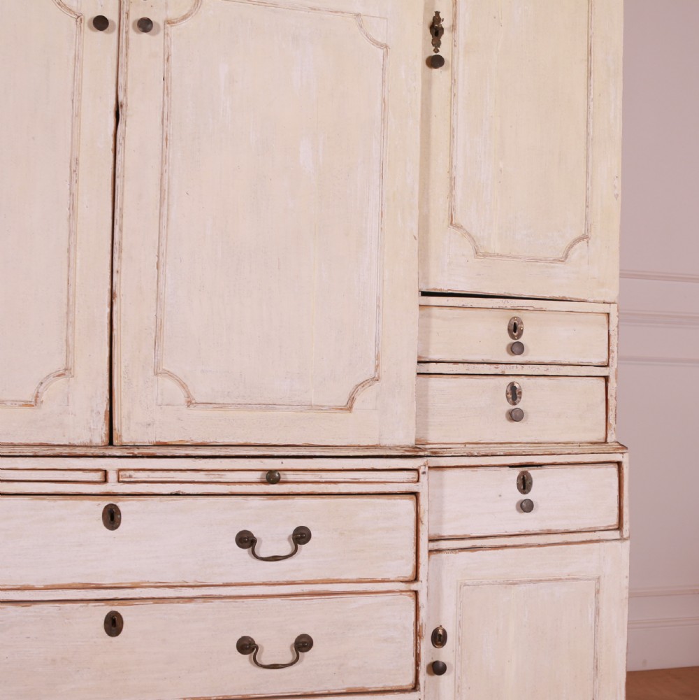 An eighteenth-century off-white painted housekeepers cupboard featuring fielded panel cupboard doors above multiple drawers with brass handles, supported by bracket feet. View V