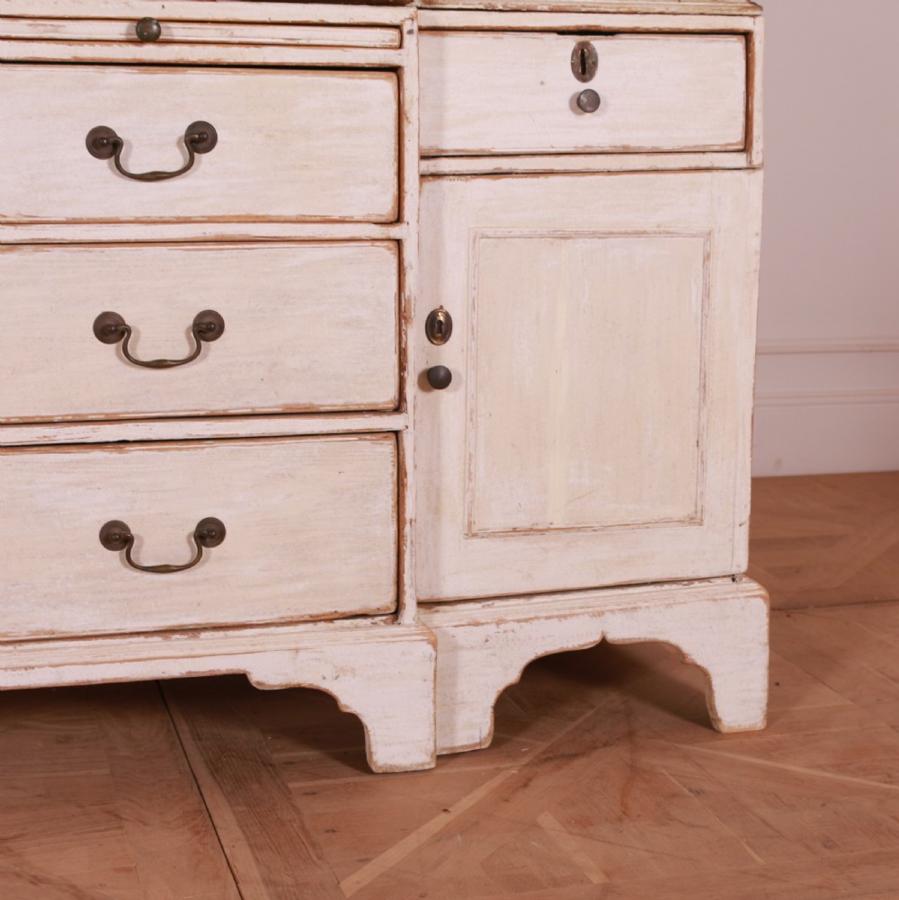 An eighteenth-century off-white painted housekeepers cupboard featuring fielded panel cupboard doors above multiple drawers with brass handles, supported by bracket feet. View VI