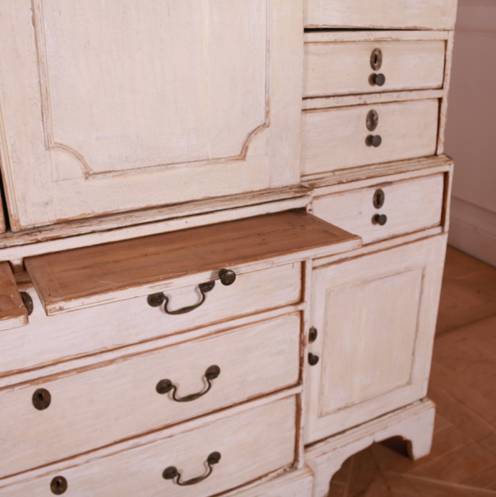 An eighteenth-century off-white painted housekeepers cupboard featuring fielded panel cupboard doors above multiple drawers with brass handles, supported by bracket feet. View VIII
