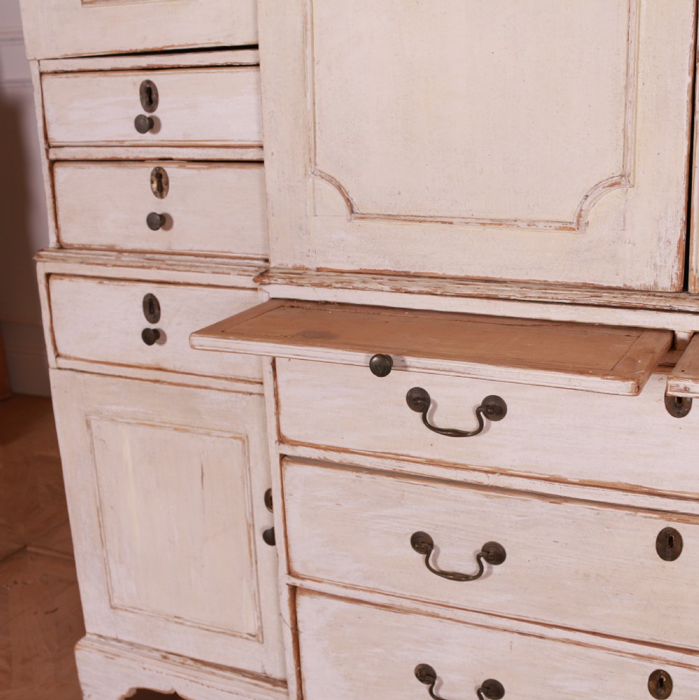 An eighteenth-century off-white painted housekeepers cupboard featuring fielded panel cupboard doors above multiple drawers with brass handles, supported by bracket feet. View IX