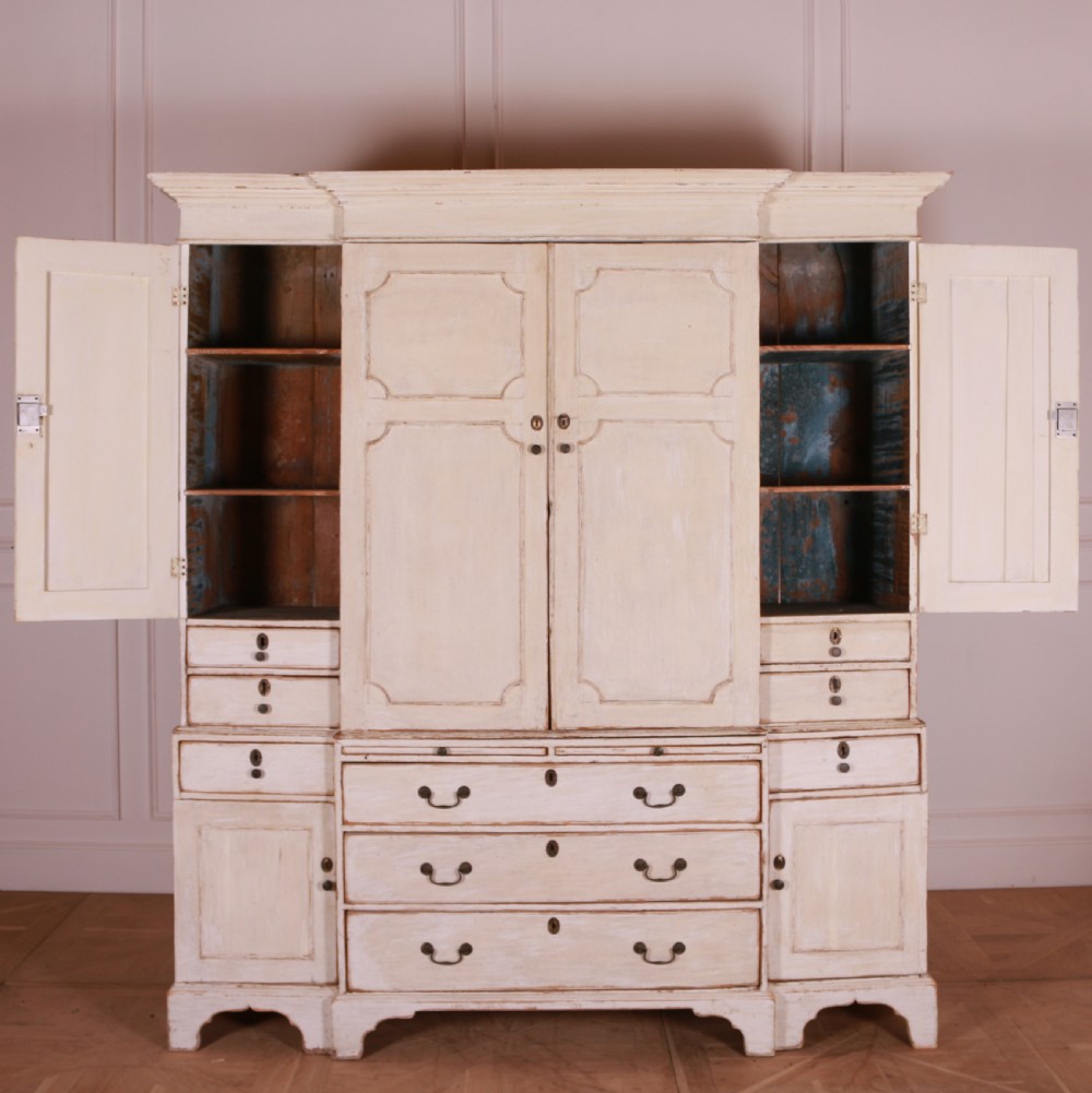 An eighteenth-century off-white painted housekeepers cupboard featuring fielded panel cupboard doors above multiple drawers with brass handles, supported by bracket feet. View X