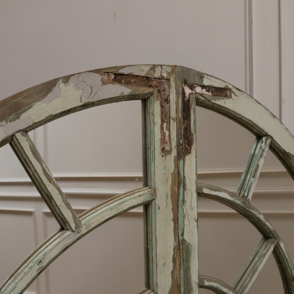 A large semi-circular arched architectural window frame with distressed green paint finish converted into a multi-pane mirror. View II