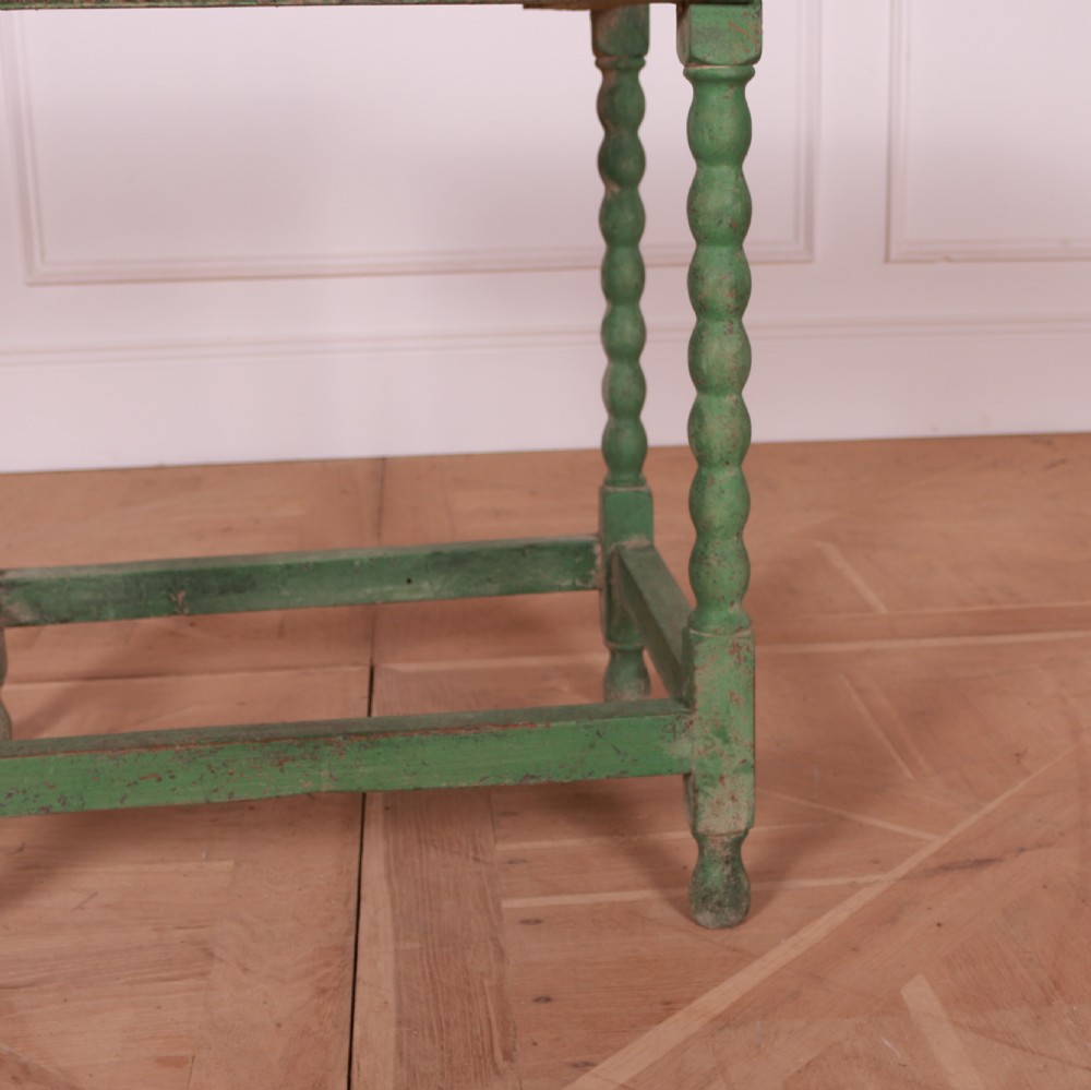 An 18th-century green painted wooden lamp table featuring four bobbin-turned legs, a rectangular top, lower stretchers, and a single drawer with a brass drop handle. View V
