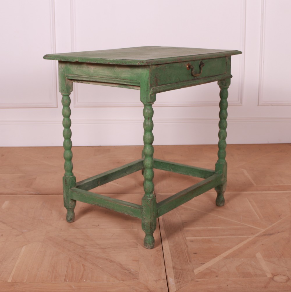 An 18th-century green painted wooden lamp table featuring four bobbin-turned legs, a rectangular top, lower stretchers, and a single drawer with a brass drop handle. View VIII