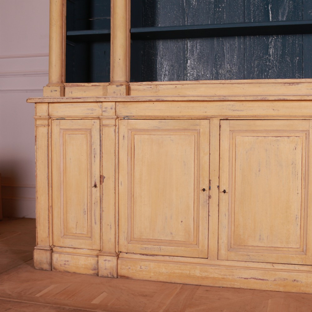 A large antique French painted bookcase featuring a pale yellow exterior, open shelving with a dark blue painted interior, and panelled cupboard doors at the base. View II