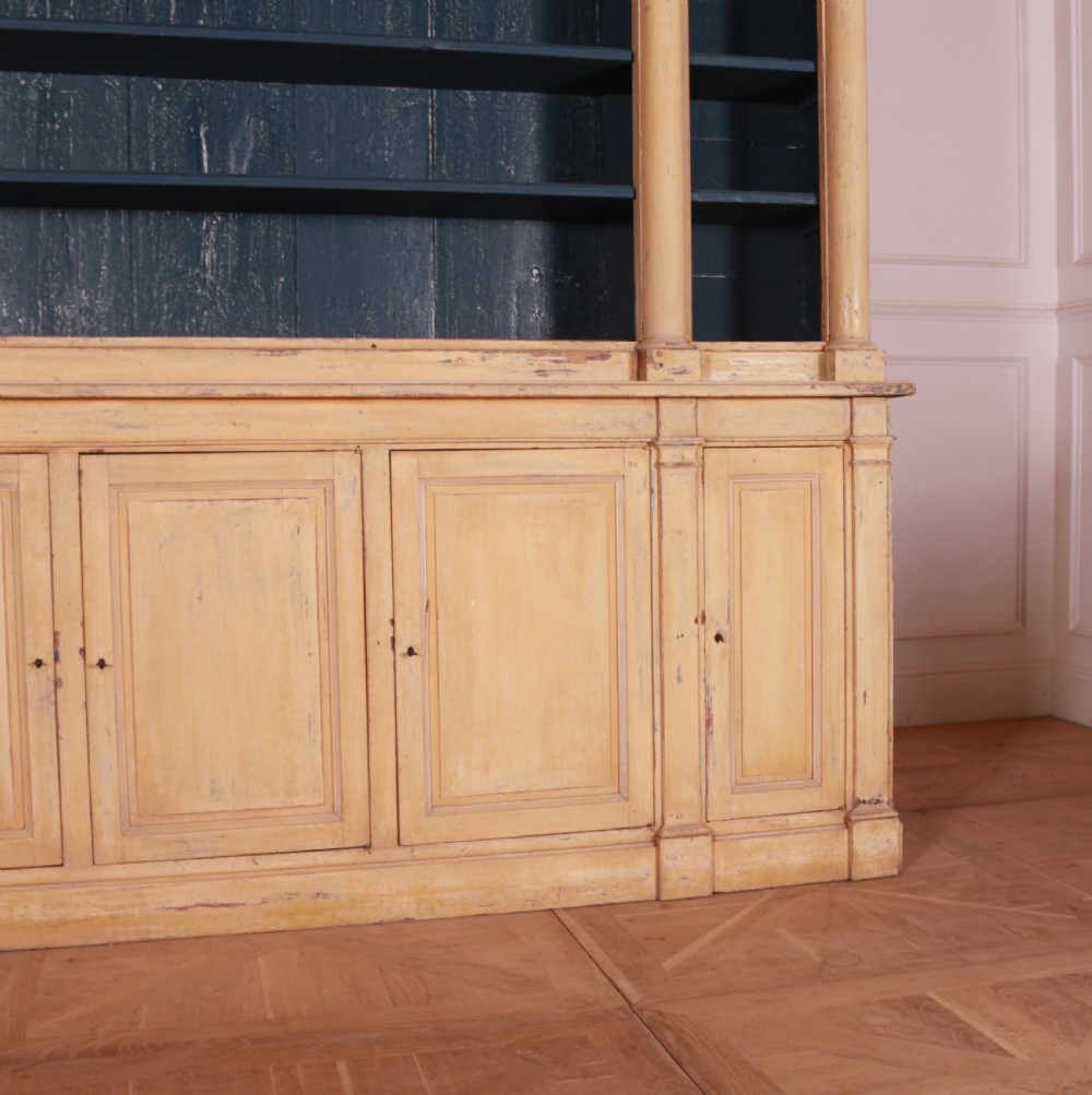 A large antique French painted bookcase featuring a pale yellow exterior, open shelving with a dark blue painted interior, and panelled cupboard doors at the base. View III