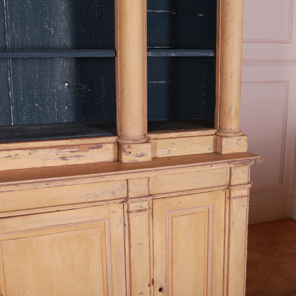 A large antique French painted bookcase featuring a pale yellow exterior, open shelving with a dark blue painted interior, and panelled cupboard doors at the base. View VI