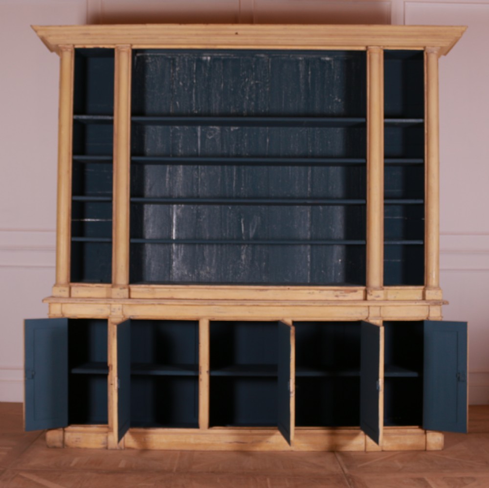 A large antique French painted bookcase featuring a pale yellow exterior, open shelving with a dark blue painted interior, and panelled cupboard doors at the base. View VII