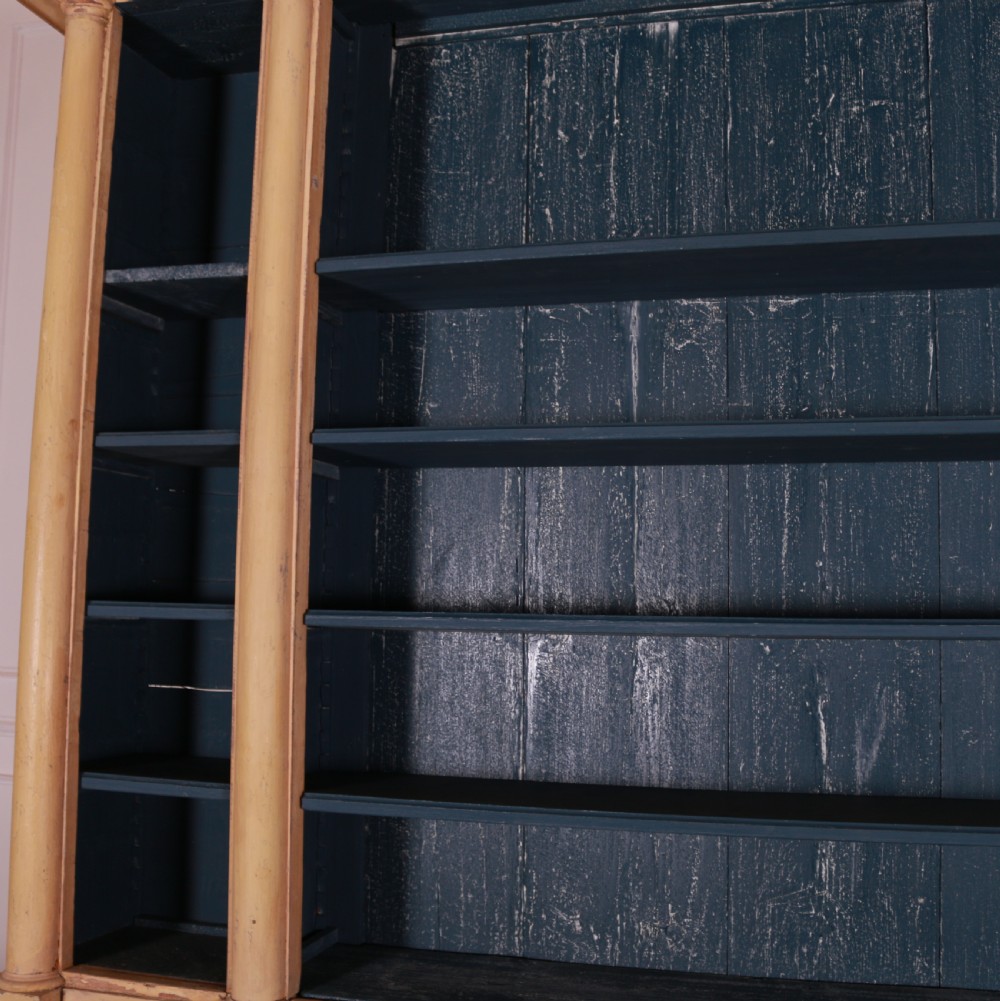 A large antique French painted bookcase featuring a pale yellow exterior, open shelving with a dark blue painted interior, and panelled cupboard doors at the base. View VIII