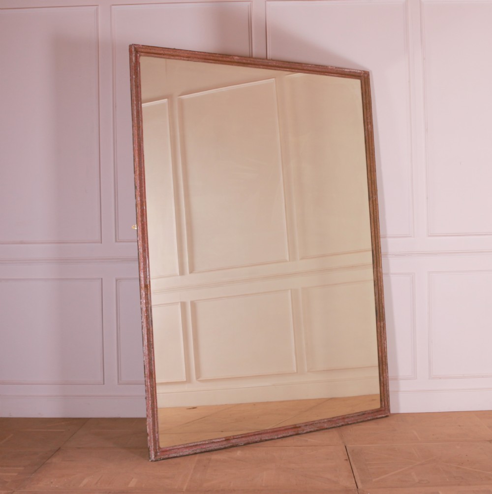 A large rectangular floor-leaning mirror featuring a distressed reddish-brown painted wooden frame and a clear reflective plate.