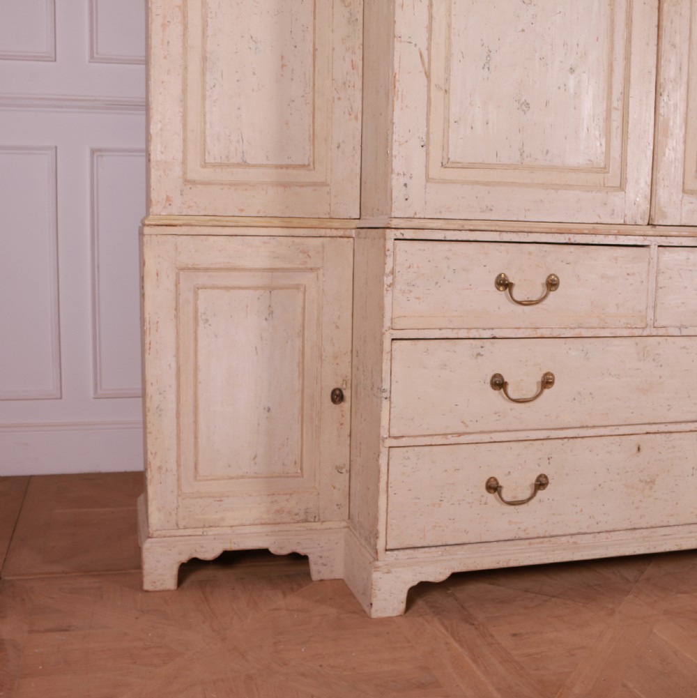 An antique cream-painted breakfront housekeepers cupboard featuring central panelled doors above drawers, flanked by tall side cupboards. View III