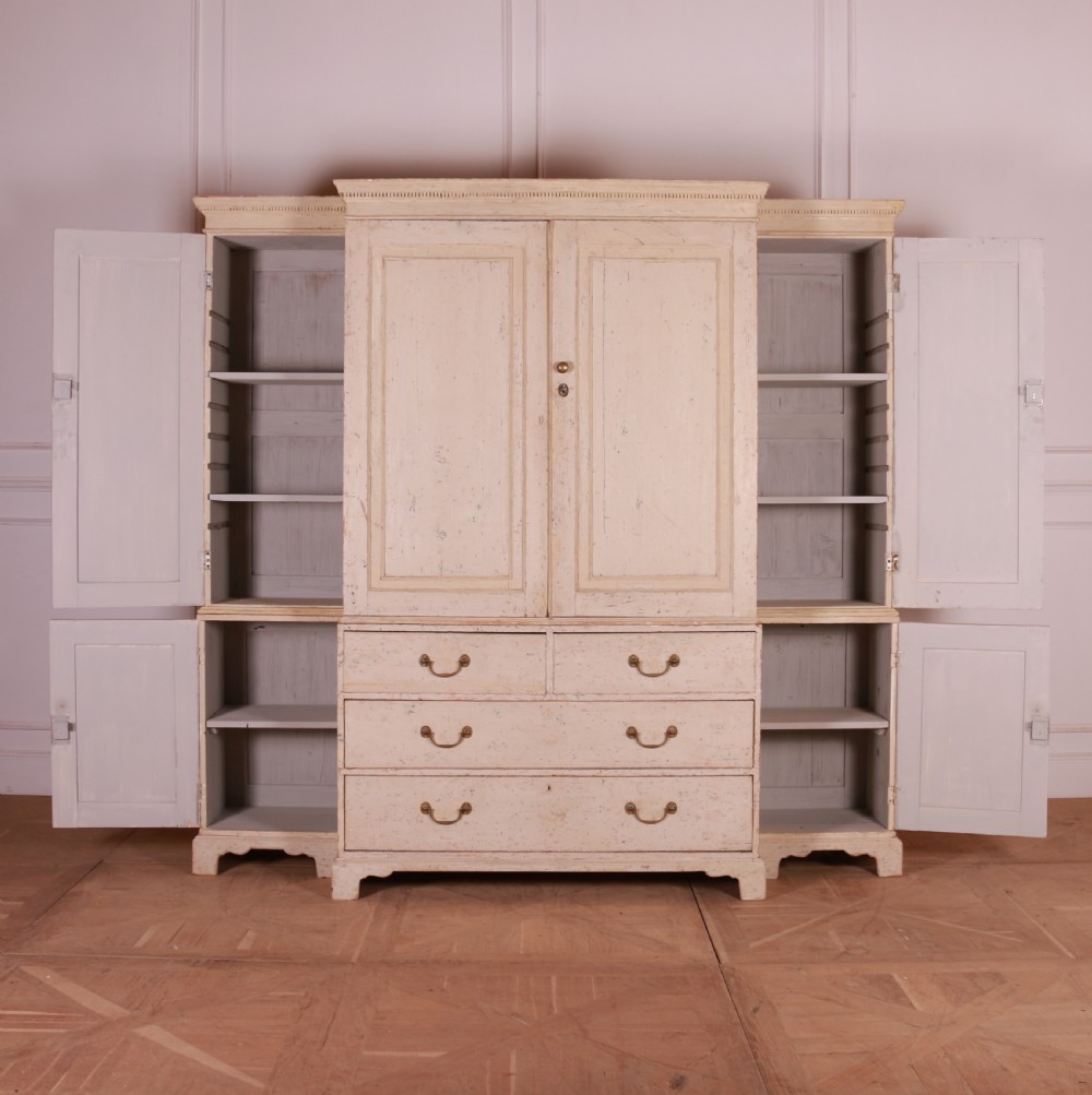 An antique cream-painted breakfront housekeepers cupboard featuring central panelled doors above drawers, flanked by tall side cupboards. View V