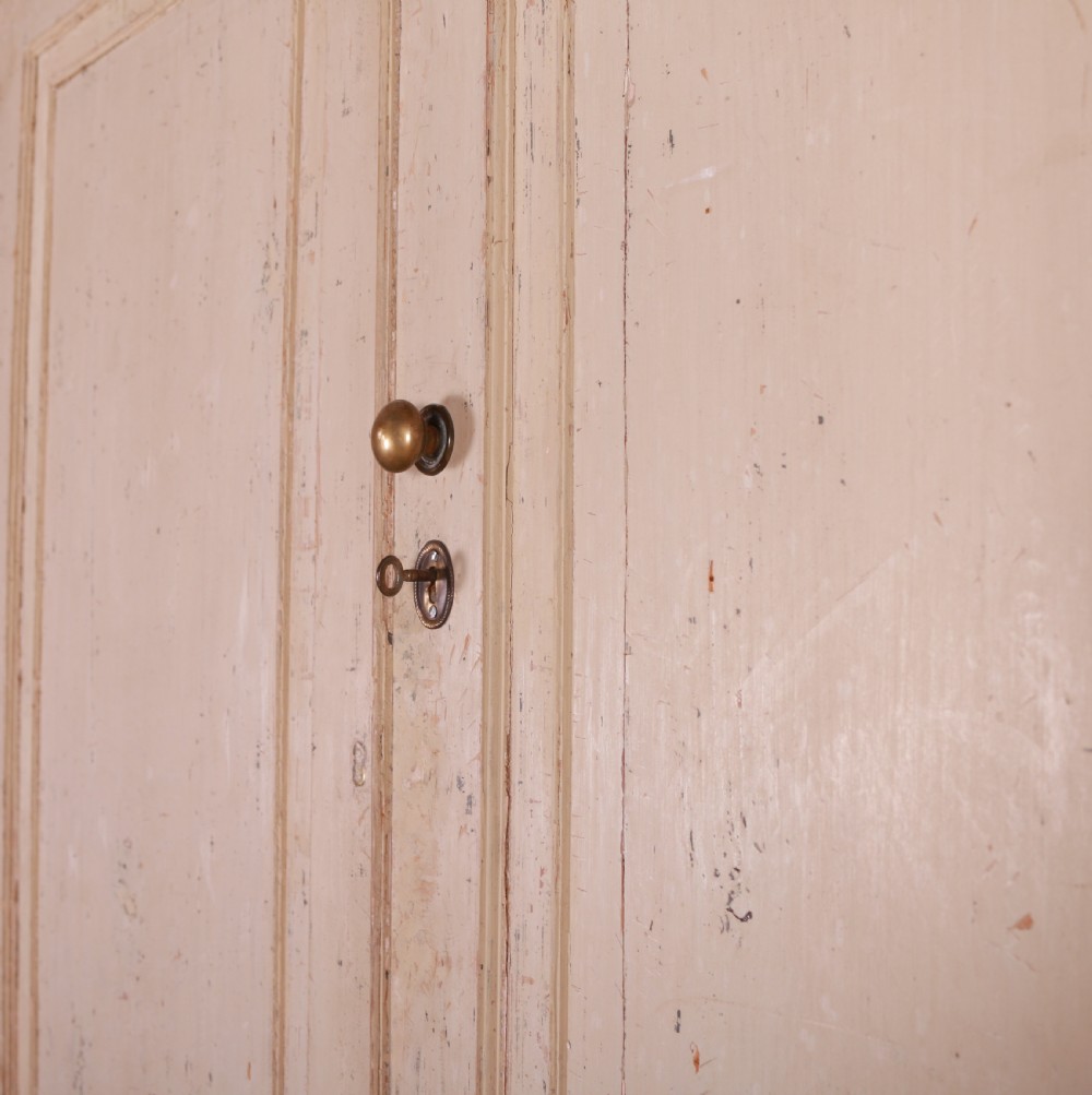 An antique cream-painted breakfront housekeepers cupboard featuring central panelled doors above drawers, flanked by tall side cupboards. View VIII