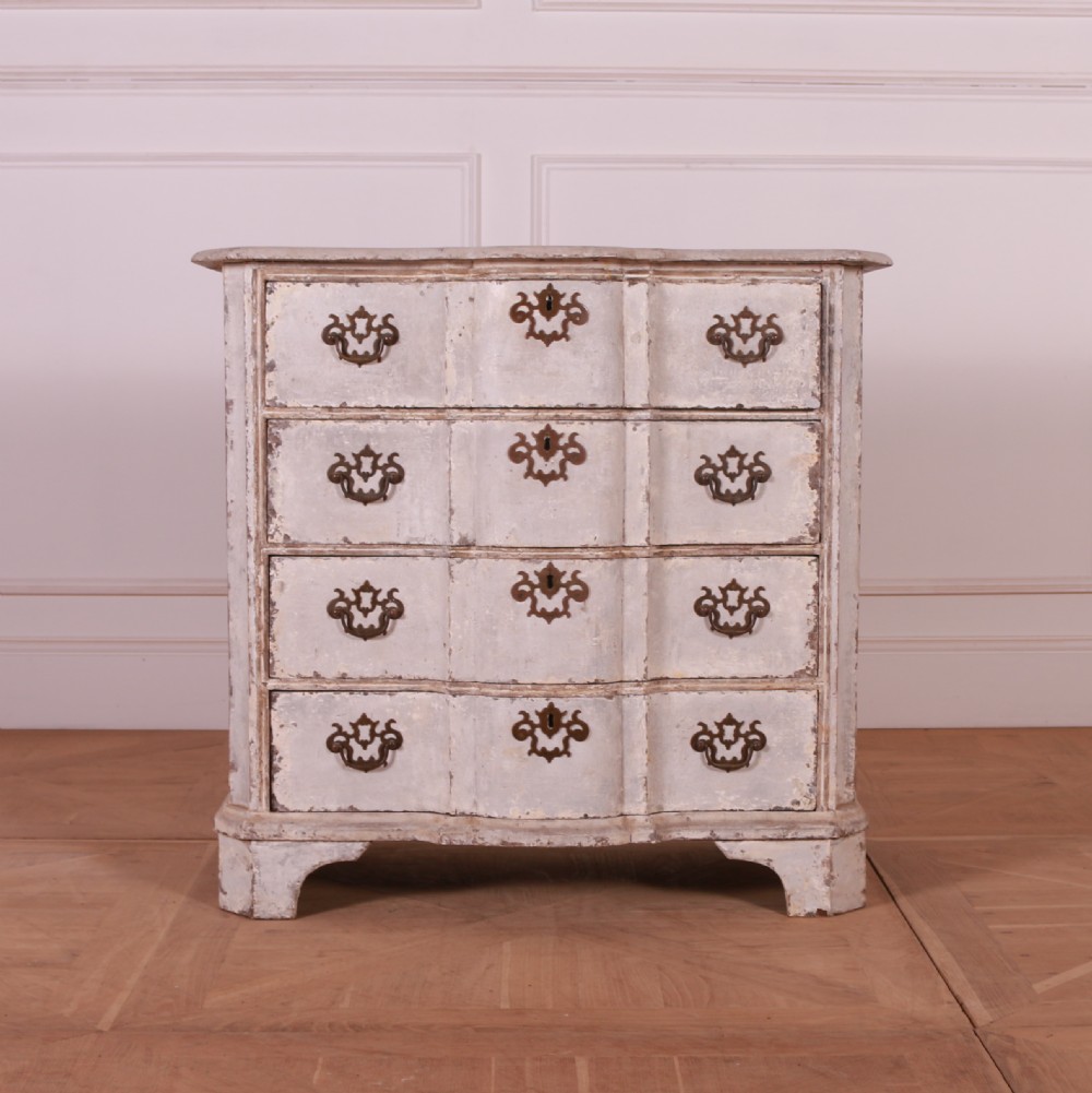 An 18th-century Dutch serpentine-front commode featuring four drawers with a distressed pale paint finish and ornate brass handles.