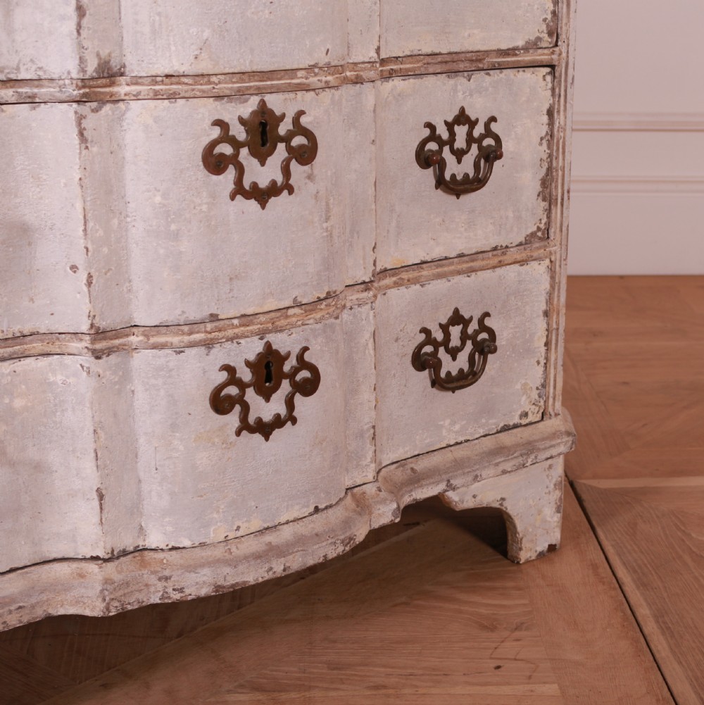 An 18th-century Dutch serpentine-front commode featuring four drawers with a distressed pale paint finish and ornate brass handles. View V