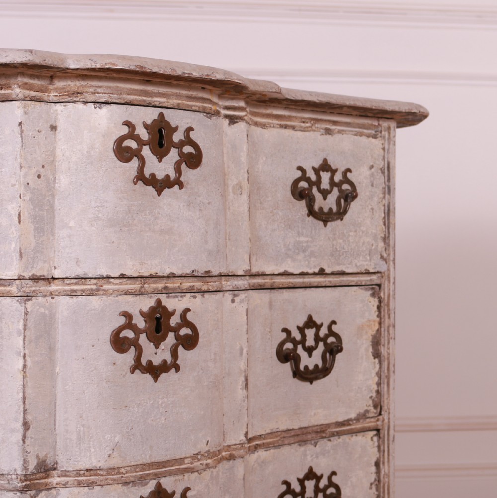 An 18th-century Dutch serpentine-front commode featuring four drawers with a distressed pale paint finish and ornate brass handles. View VI