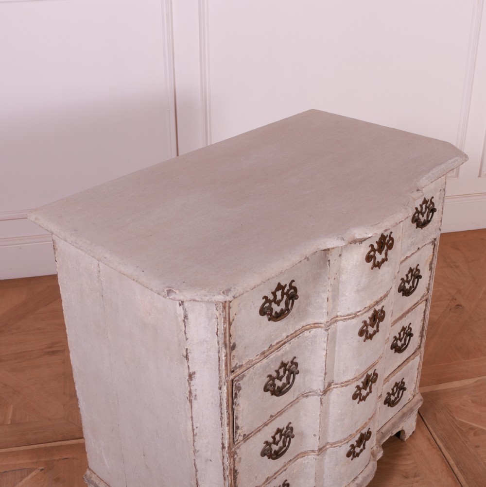An 18th-century Dutch serpentine-front commode featuring four drawers with a distressed pale paint finish and ornate brass handles. View VII