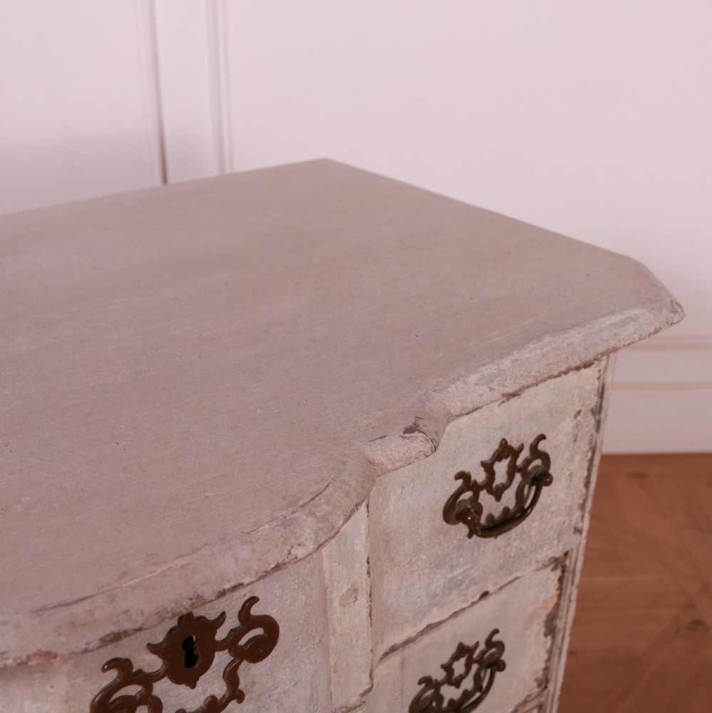 An 18th-century Dutch serpentine-front commode featuring four drawers with a distressed pale paint finish and ornate brass handles. View IX