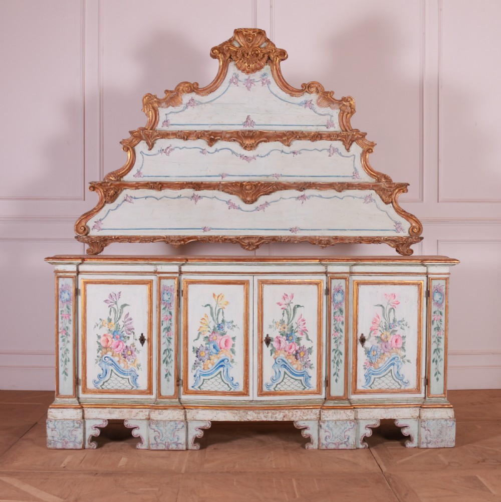 An 18th-century Italian painted credenza featuring four floral-panel doors, giltwood mouldings, and a matching stepped shelf structure mounted above.