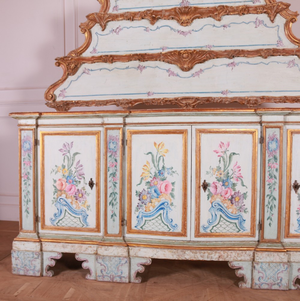An 18th-century Italian painted credenza featuring four floral-panel doors, giltwood mouldings, and a matching stepped shelf structure mounted above. View II