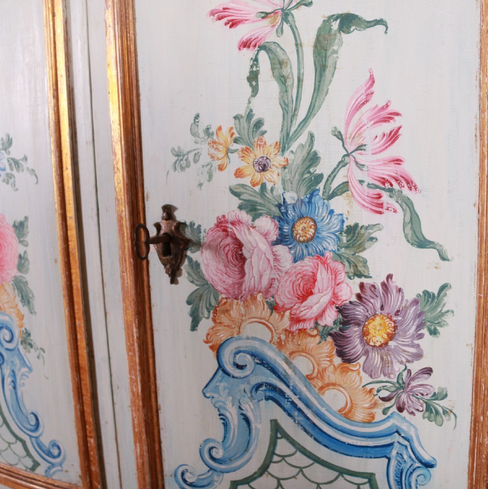 An 18th-century Italian painted credenza featuring four floral-panel doors, giltwood mouldings, and a matching stepped shelf structure mounted above. View V
