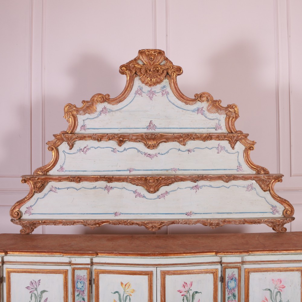 An 18th-century Italian painted credenza featuring four floral-panel doors, giltwood mouldings, and a matching stepped shelf structure mounted above. View VII