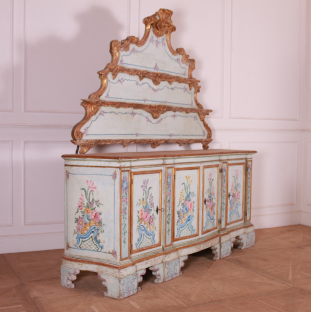 An 18th-century Italian painted credenza featuring four floral-panel doors, giltwood mouldings, and a matching stepped shelf structure mounted above. View X