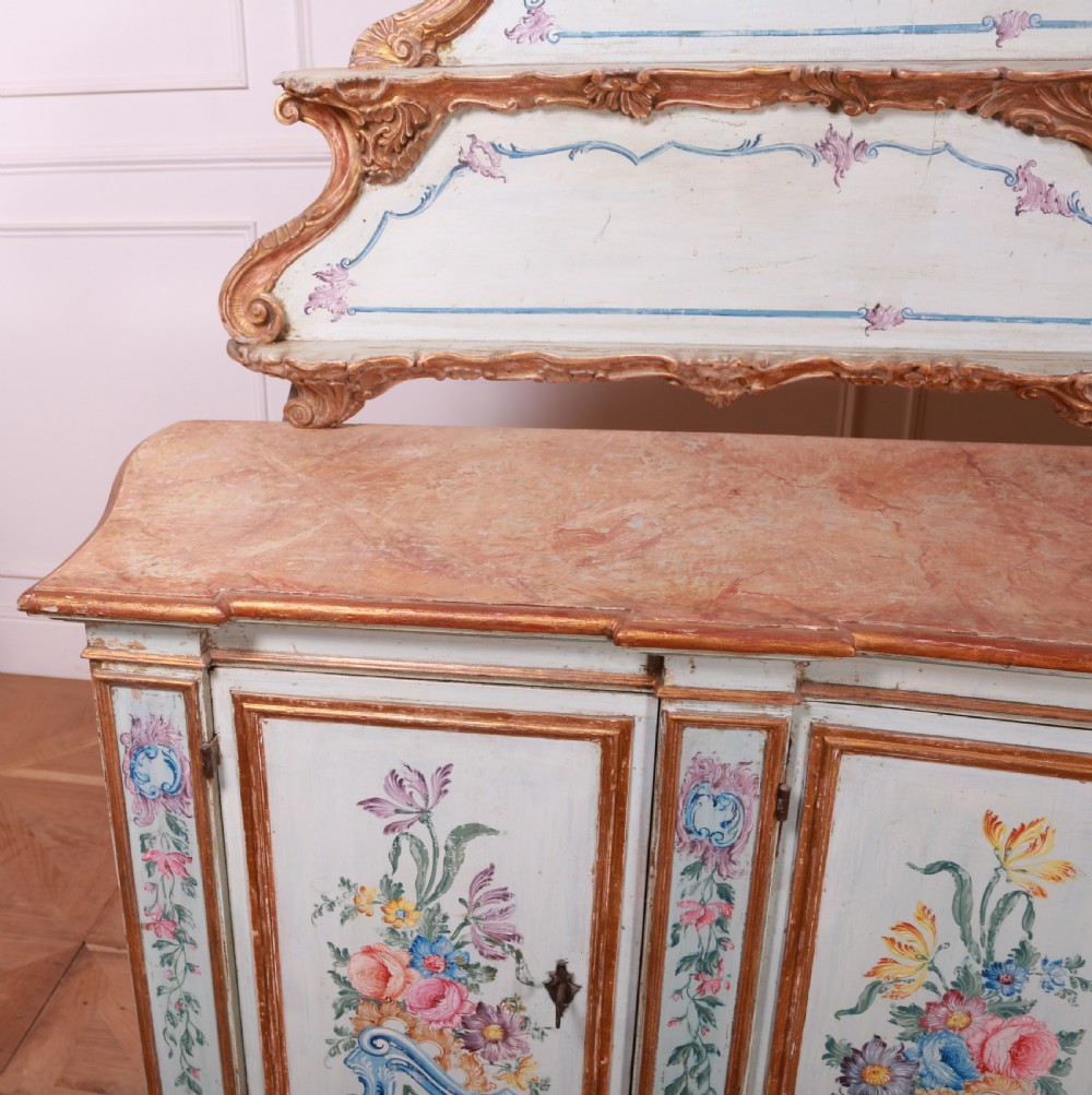 An 18th-century Italian painted credenza featuring four floral-panel doors, giltwood mouldings, and a matching stepped shelf structure mounted above. View XVI