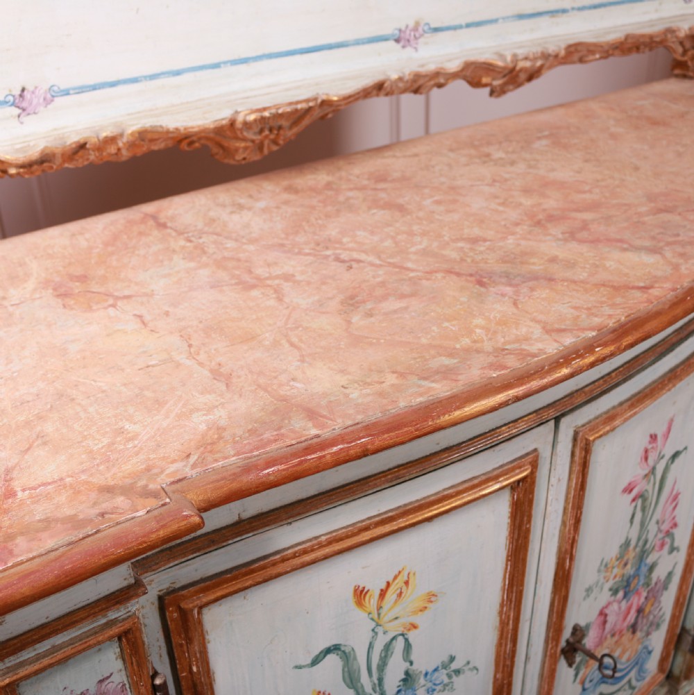 An 18th-century Italian painted credenza featuring four floral-panel doors, giltwood mouldings, and a matching stepped shelf structure mounted above. View XVIII