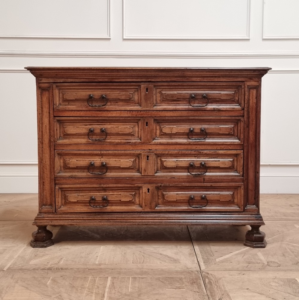 An 18th-century Italian walnut commode featuring four long drawers with geometric raised panel mouldings, iron drop handles, and octagonal feet.