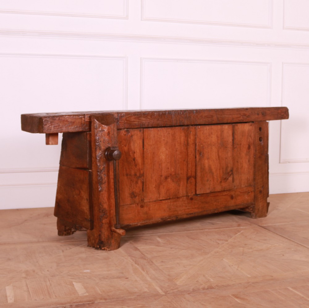 A rustic French primitive timber workbench with an integrated wooden vice mechanism and a thick slab top.